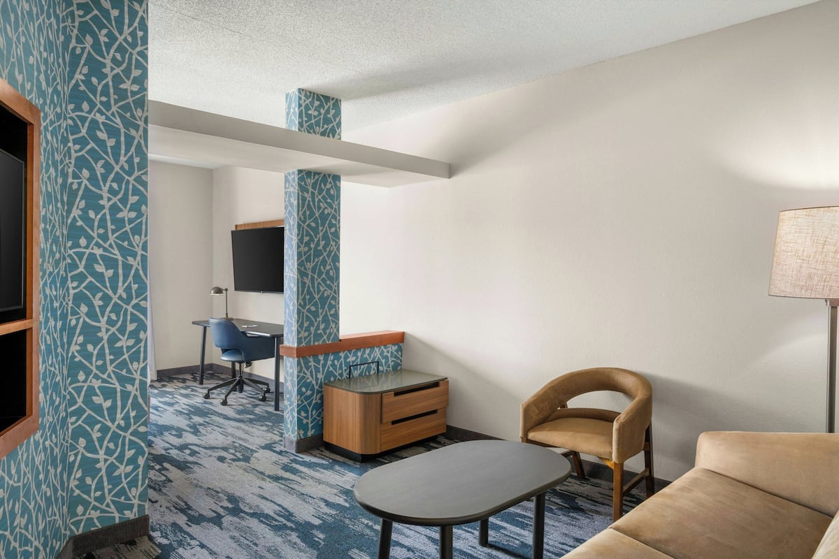 Een moderne hotelkamer met een blauw patroon op de muur, een houten bureau met stoel, een bank en een lamp.