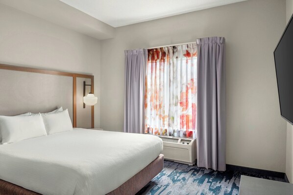 A hotel room with a large bed, a window with curtains, a wall-mounted TV, and a ceiling light.