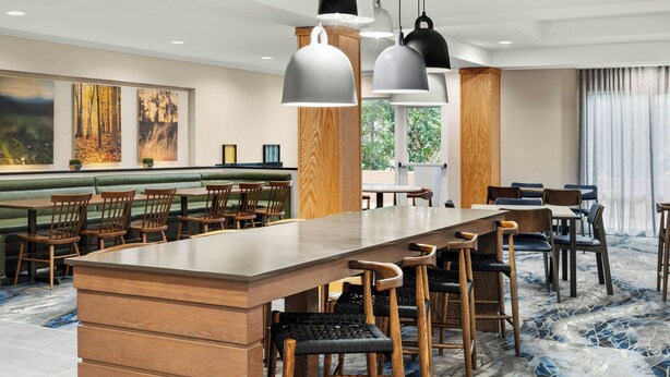 Eine moderne Hotelhalle mit einer langen Bar, Holzsesseln und Pendelleuchten.