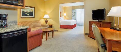 A hotel room with a kitchenette, a bed, a desk, and a television.