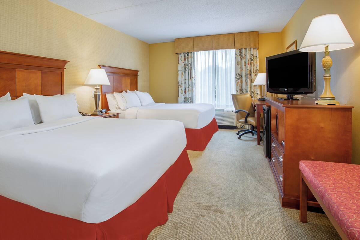 Ein Hotelzimmer mit zwei Betten, einem Schreibtisch mit Fernseher und einem Sessel.