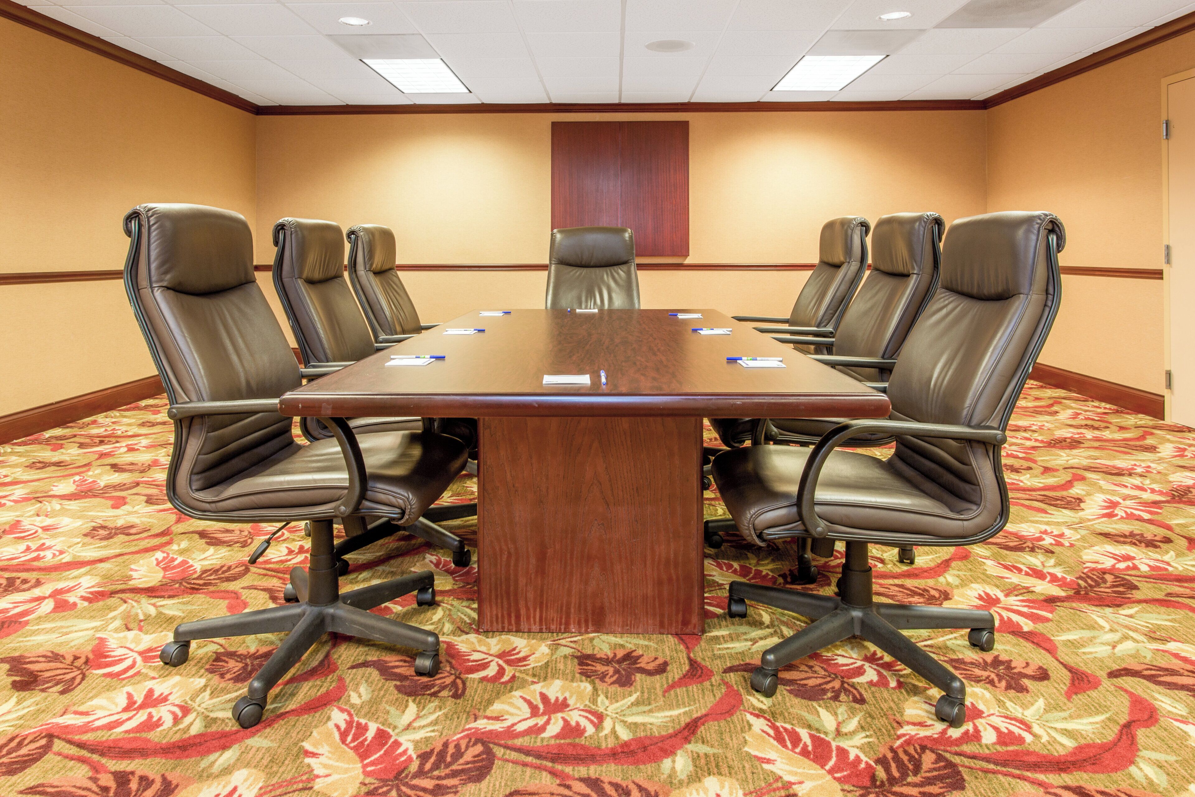 A conference room with a large table surrounded by leather chairs, a carpeted floor, and a wooden panel on the wall.