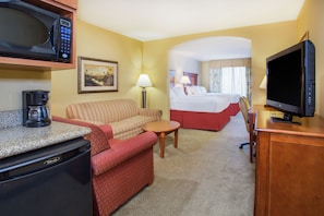 Quarto de hotel com cozinha compacta, uma cama, televisão e sofá.