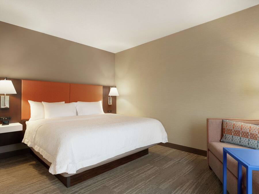 Et hotelværelse med en stor seng, to sengeborde med lamper, en lille sofa med en mønstret pude og et blåt bord.