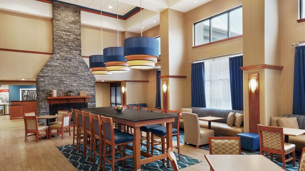 A spacious hotel lobby with a large stone fireplace, multiple seating areas including a sofa and tables, and a view of the outdoors through large windows. - Hampton Inn & Suites Ephrata - Mountain Springs (Ephrata)