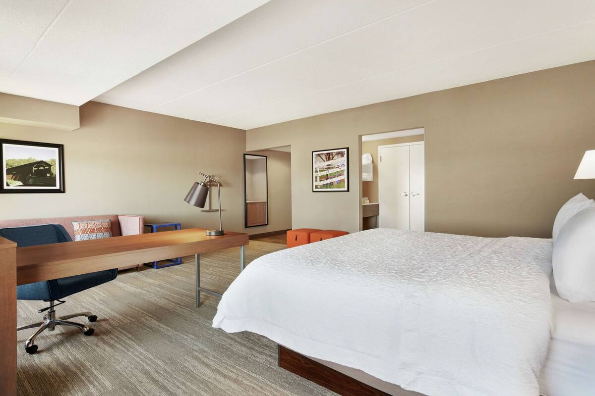 A hotel room with a large bed, a desk with a chair, a sofa, and two framed pictures on the wall.