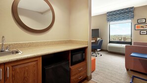 A compact hotel room with a kitchenette, a round mirror, a window with a view, and a seating area with a chair and a small table. - Hampton Inn & Suites Ephrata - Mountain Springs (Ephrata)
