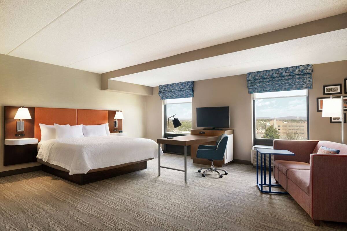 A hotel room with a bed, desk, chair, and sofa.