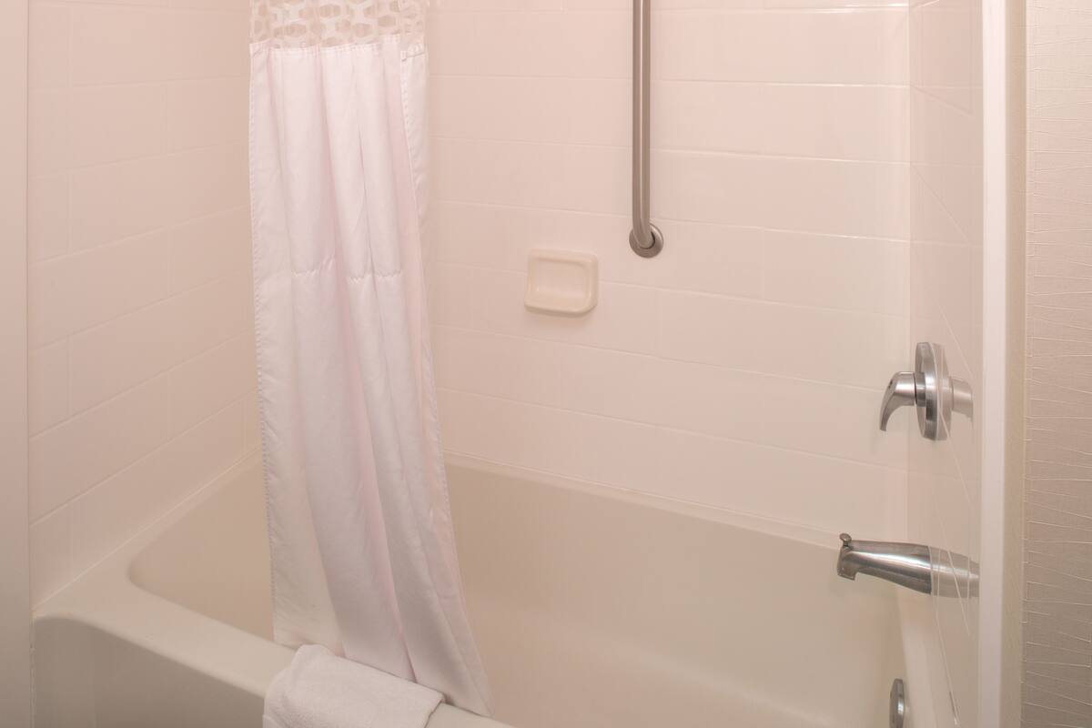 A white bathtub with a shower curtain, a handheld showerhead, and a soap dish on the wall.