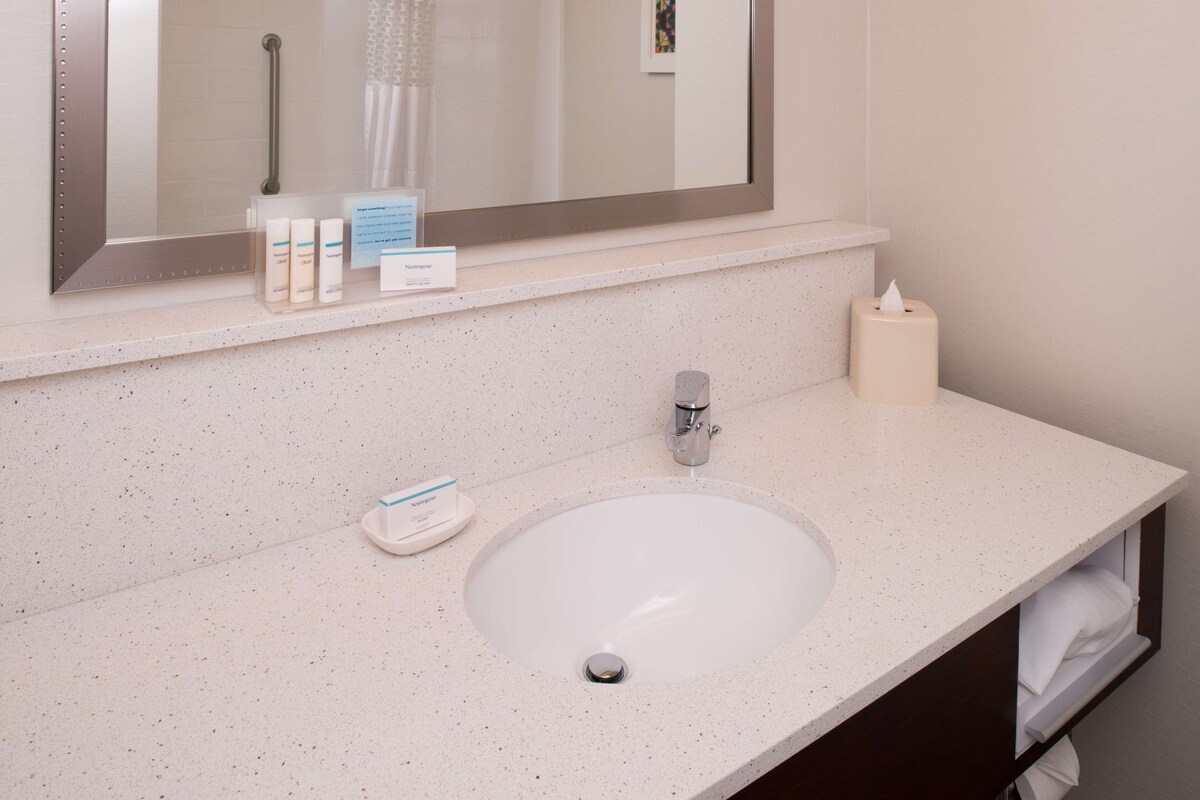 A bathroom with a white sink, a mirror, a towel rack, and a soap dispenser.