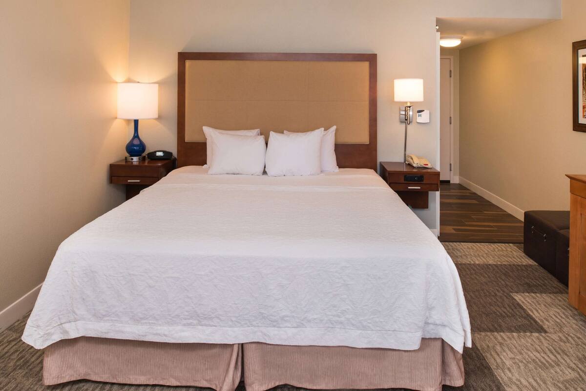 A hotel room with a large bed, two bedside tables, a nightstand, a lamp, and a wall-mounted phone.