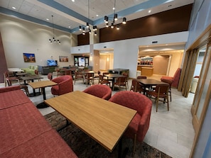 A modern dining area with multiple tables and chairs, a television, and a counter with a menu. - Hampton Inn & Suites Schertz (Schertz)