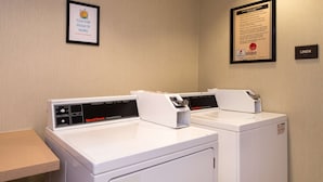 Two white commercial dryers in a laundry room with a framed safety notice on the wall and a linen sign. - Hampton Inn & Suites Schertz (Schertz)