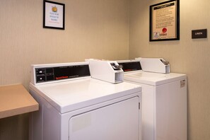 Two white commercial dryers in a laundry room with a framed safety notice on the wall and a linen sign. - Hampton Inn & Suites Schertz (Schertz)