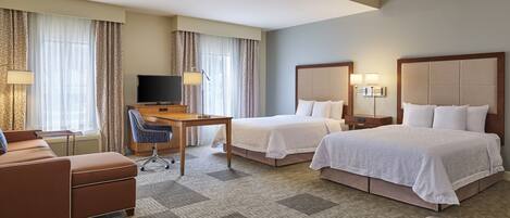 A hotel room with two beds, a desk, a TV, and a sofa.