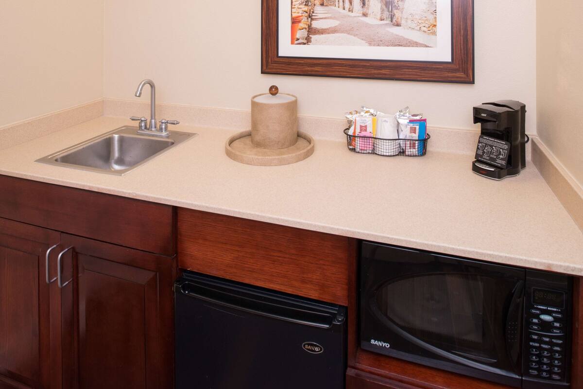 A kitchen with a sink, a coffee maker, a microwave, and a framed picture on the wall.