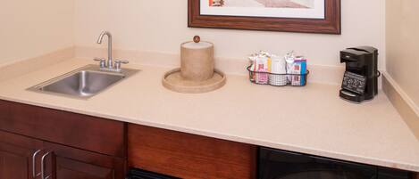 A kitchen with a sink, a coffee maker, a microwave, and a framed picture on the wall.