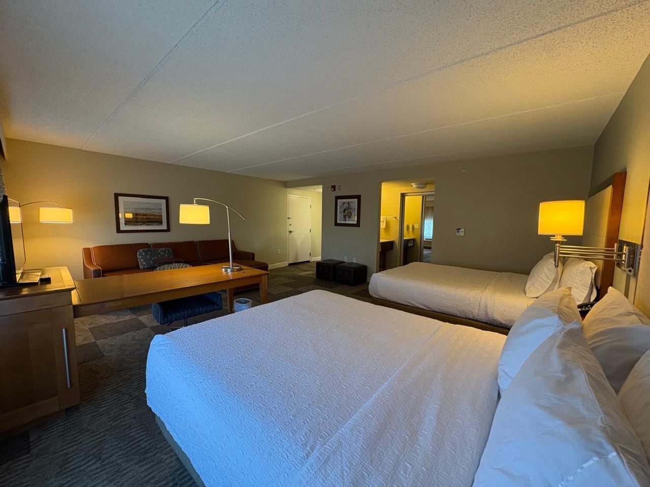 Habitación de hotel con una cama grande, una cama más pequeña, un escritorio, una silla y dos lámparas.