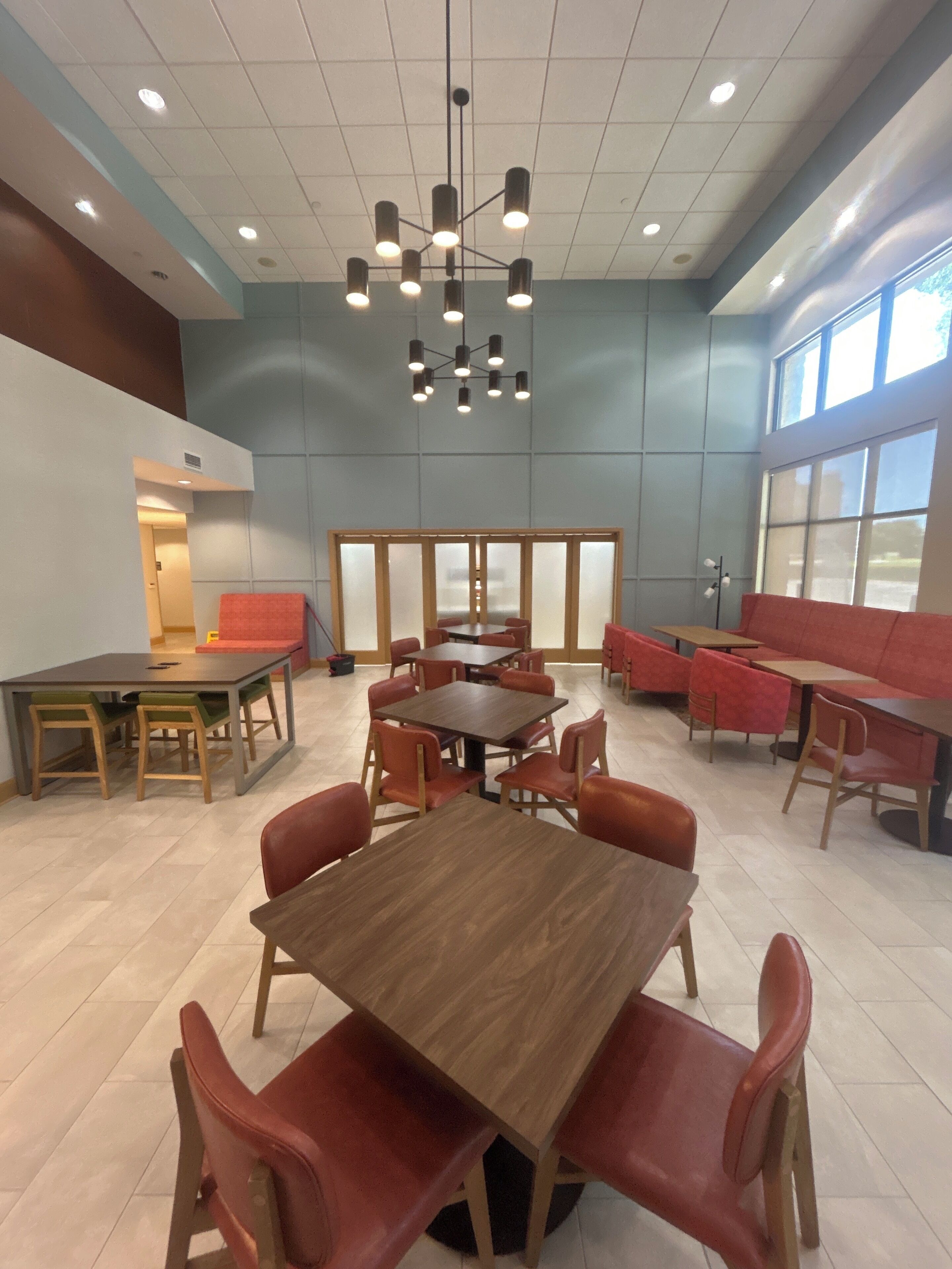 A spacious indoor area with multiple seating arrangements, including tables and chairs, and a large window providing natural light.