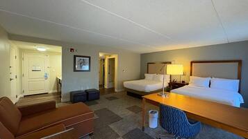 Quarto de hotel com cama, escrivaninha, cadeira e uma pequena cozinha.