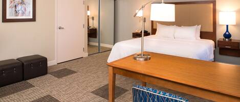A hotel room with a bed, bedside table, lamp, chair, and a door leading to a bathroom.