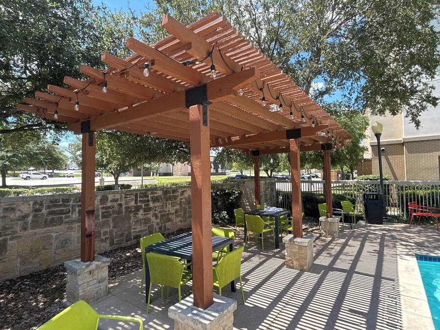 Um pátio externo com pérgola, paredes de pedra e mobiliário para área externa.