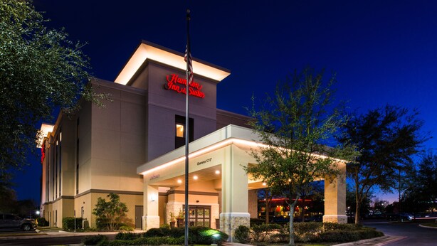 A hotel with a modern design, featuring a prominent entrance, a well-lit facade, and a flagpole. - Hampton Inn & Suites Schertz (Schertz)