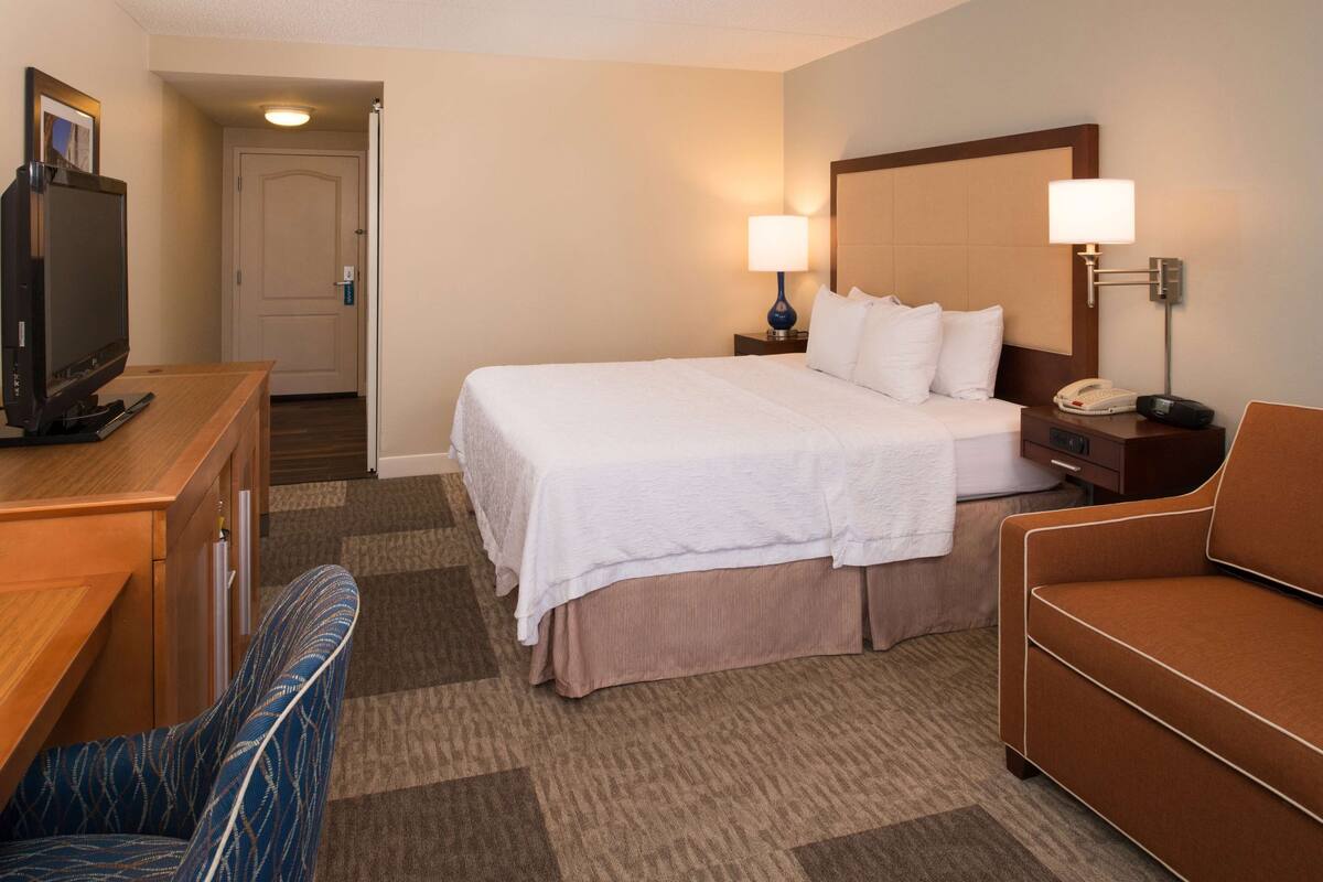 A hotel room with a bed, bedside lamps, a desk with a television, and a chair.