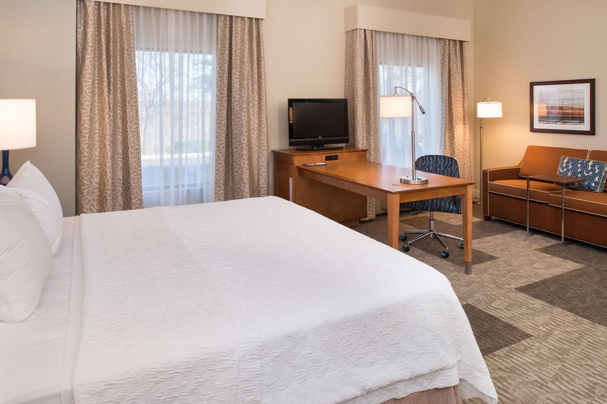 A hotel room with a large bed, a desk with a television, a chair, a sofa, and a lamp.