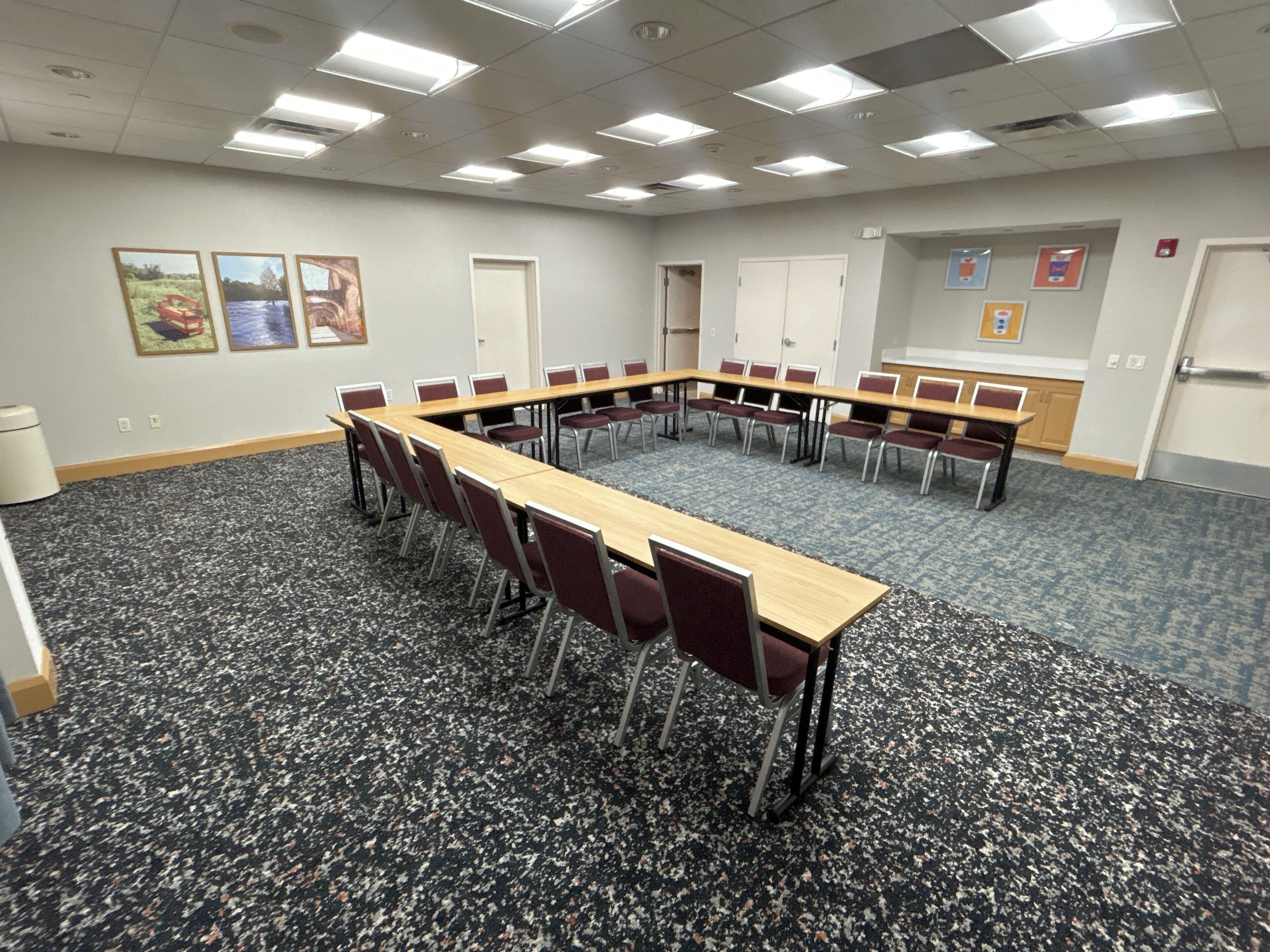 Ein Konferenzraum mit langem Tisch, Stühlen, Teppichboden und Deckenleuchten.
