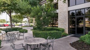 An outdoor patio area with tables and chairs, surrounded by greenery and a building entrance. - Hampton Inn & Suites Schertz (Schertz)