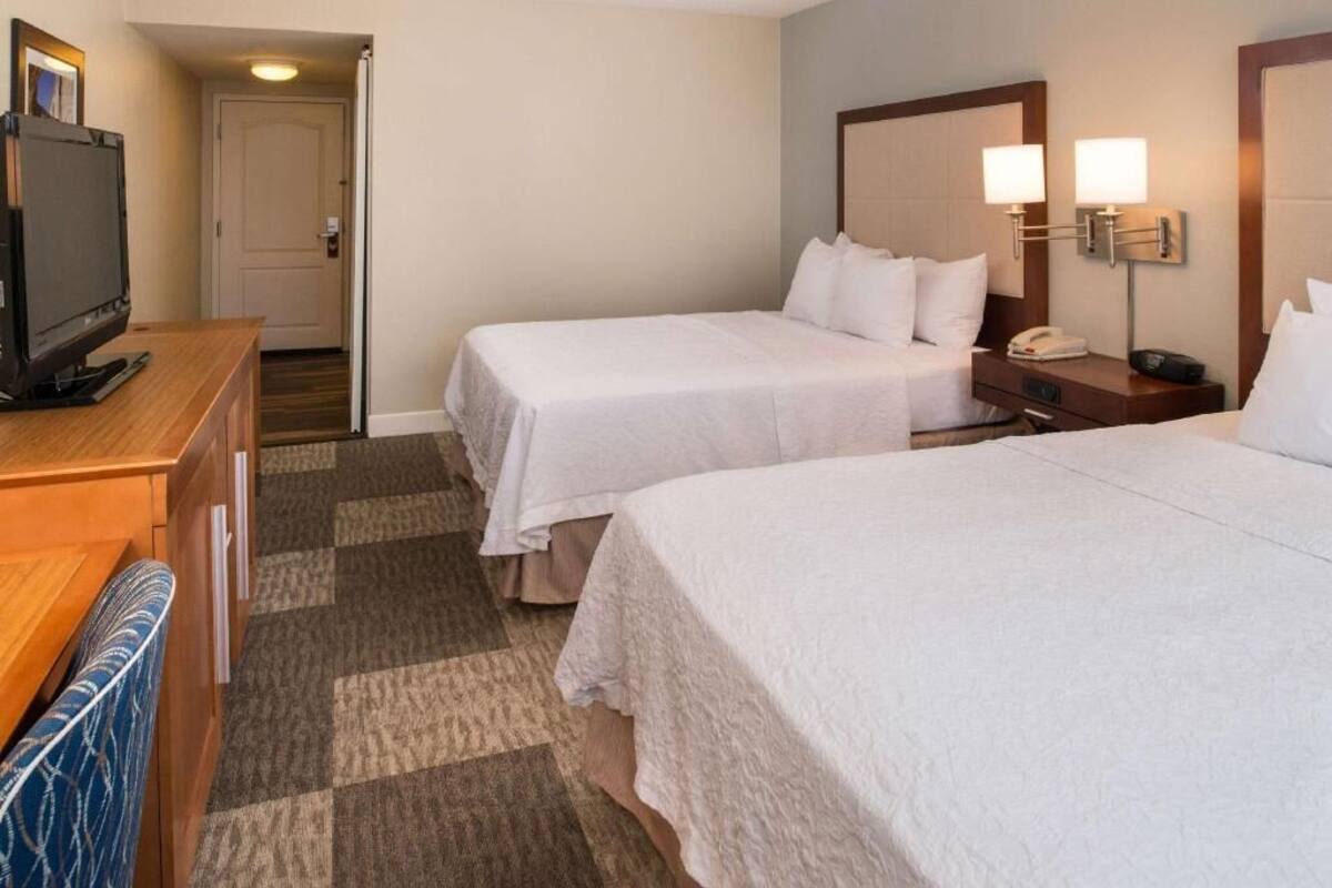 A hotel room with two beds, a TV, a desk, and a lamp.