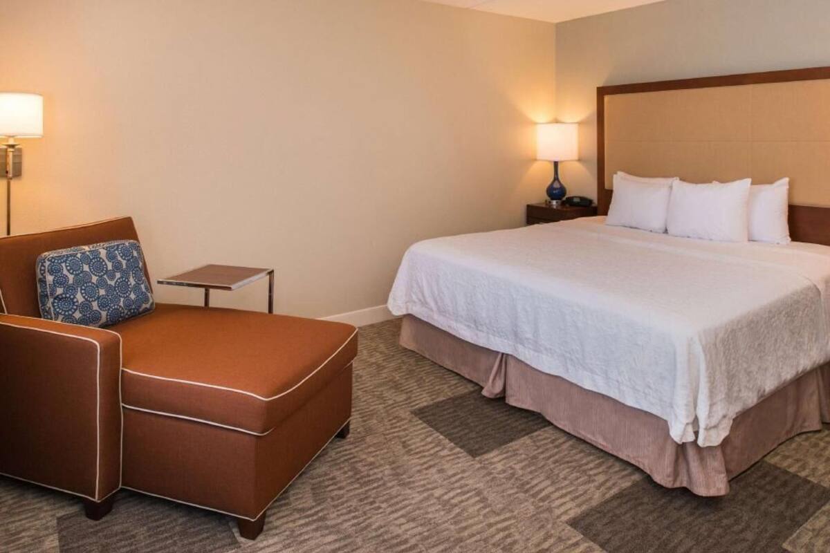 A hotel room with a bed, a brown armchair, a small table, and two wall-mounted lamps.