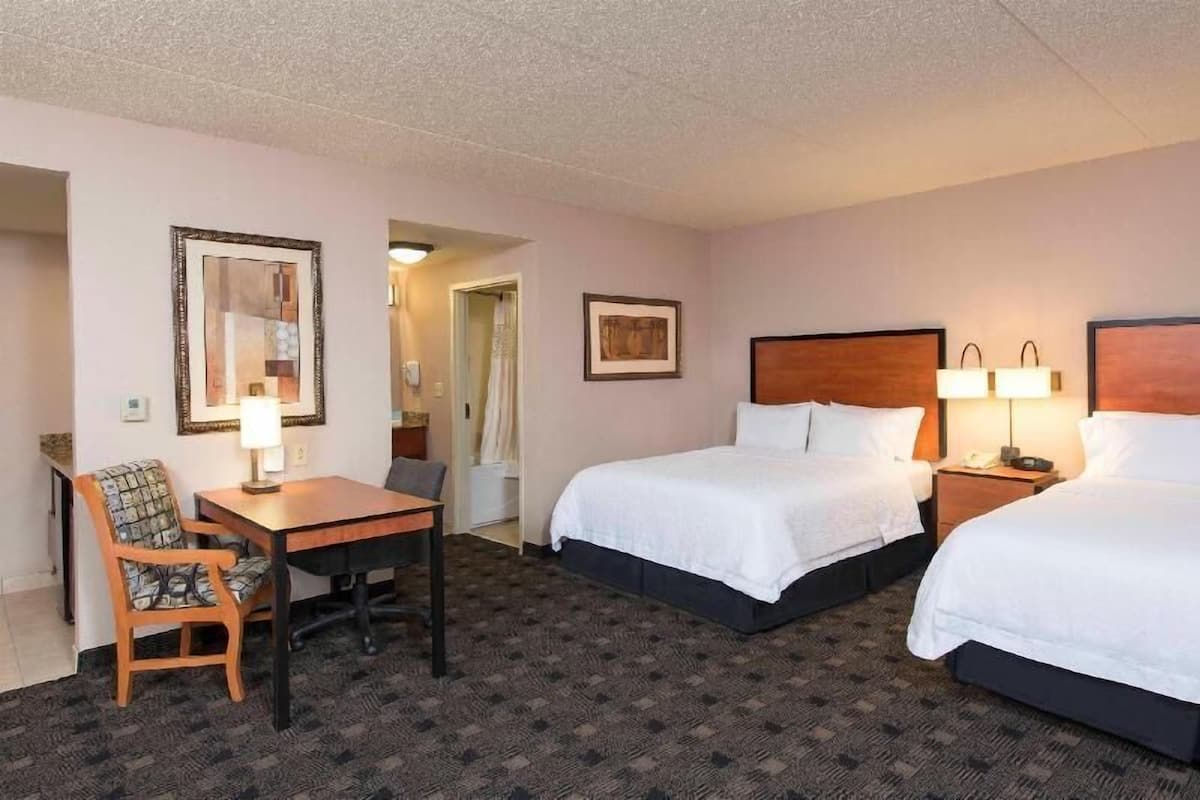 A hotel room with two beds, a desk with a chair, and a small table.