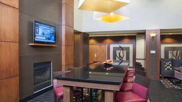 A conference room with a glass table, red chairs, a fireplace, and a television on the wall.