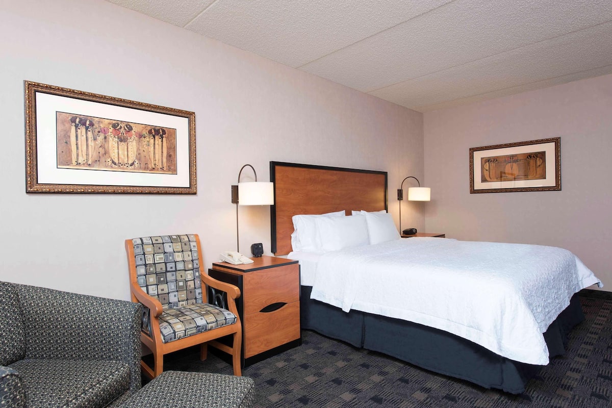 A hotel room with a bed, a chair, a nightstand, and two wall-mounted lamps.