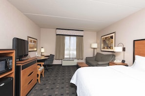 Une chambre d’hôtel équipée d’un lit, d’un bureau, d’une chaise, d’une télévision, d’un four à micro-ondes, d’une lampe et d’un tableau encadré au mur.