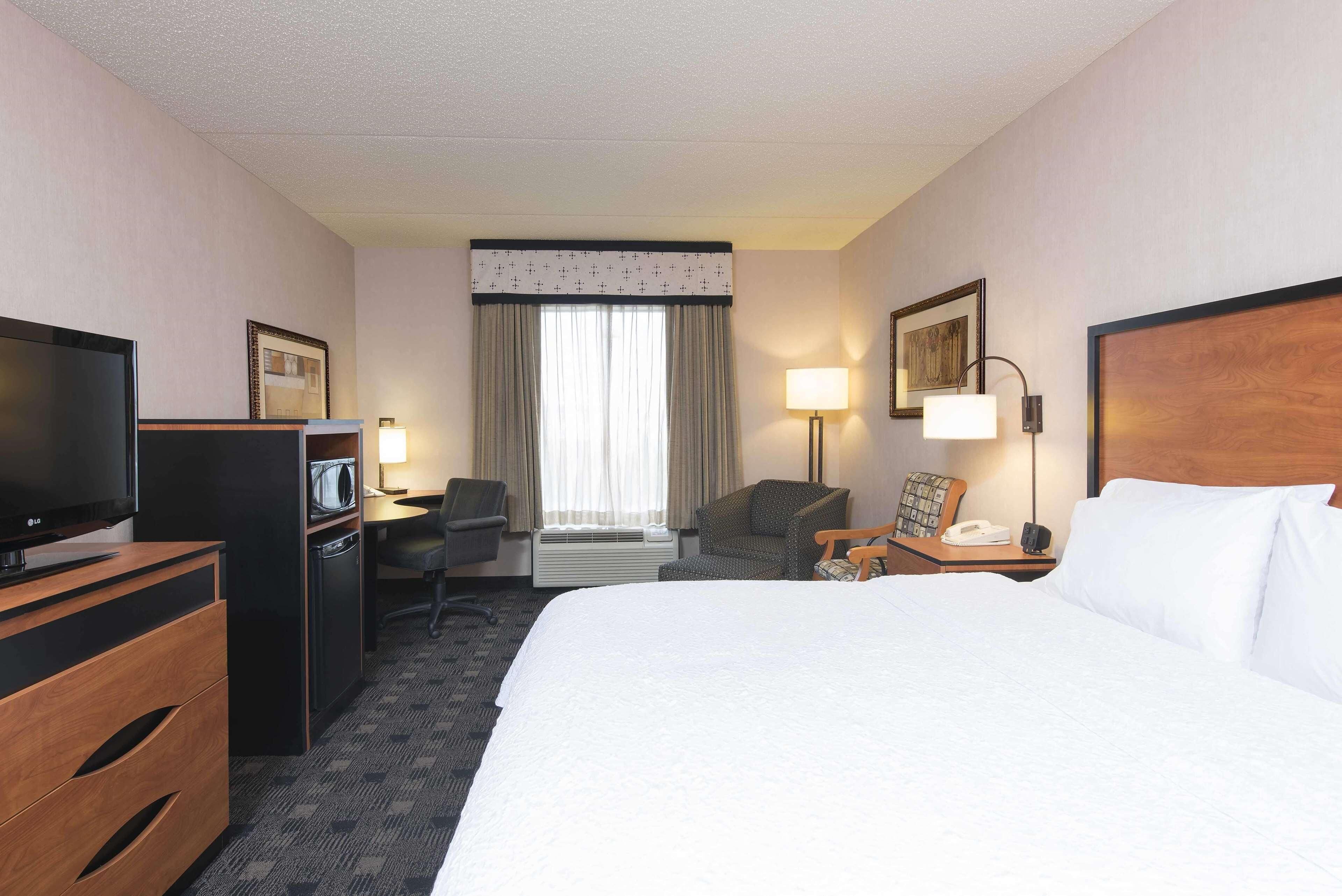 A hotel room with a bed, a desk, a television, a chair, a lamp, and a nightstand.
