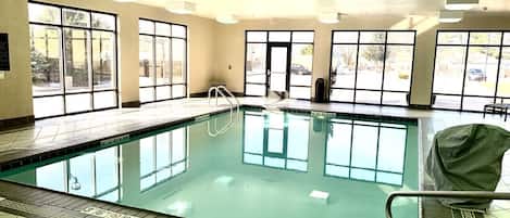 Una piscina interior con paredes de vidrio transparente, suelo de baldosas y una silla para salvavidas.