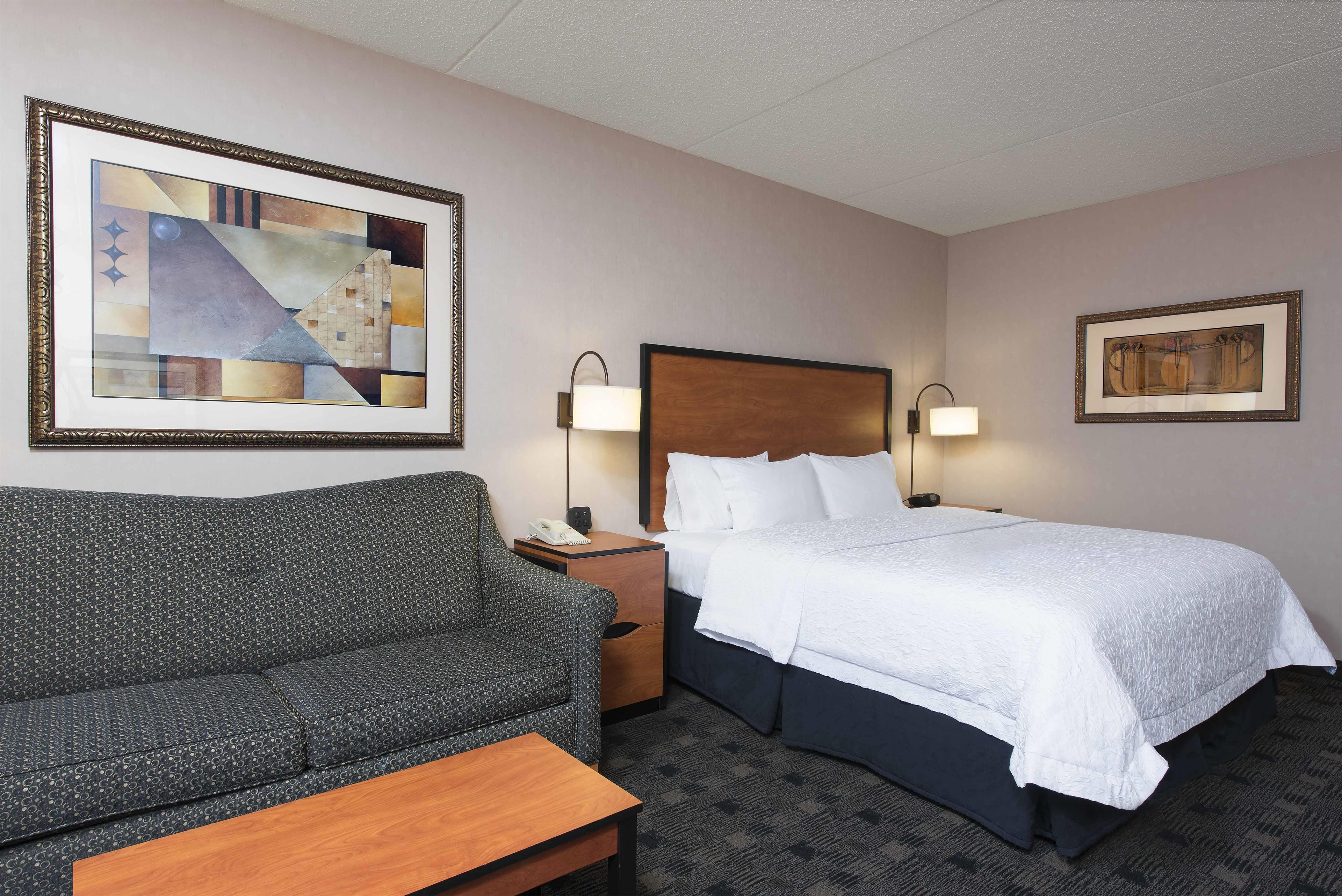 Habitación de hotel con cama, sofá, mesita de noche y dos lámparas de pared.