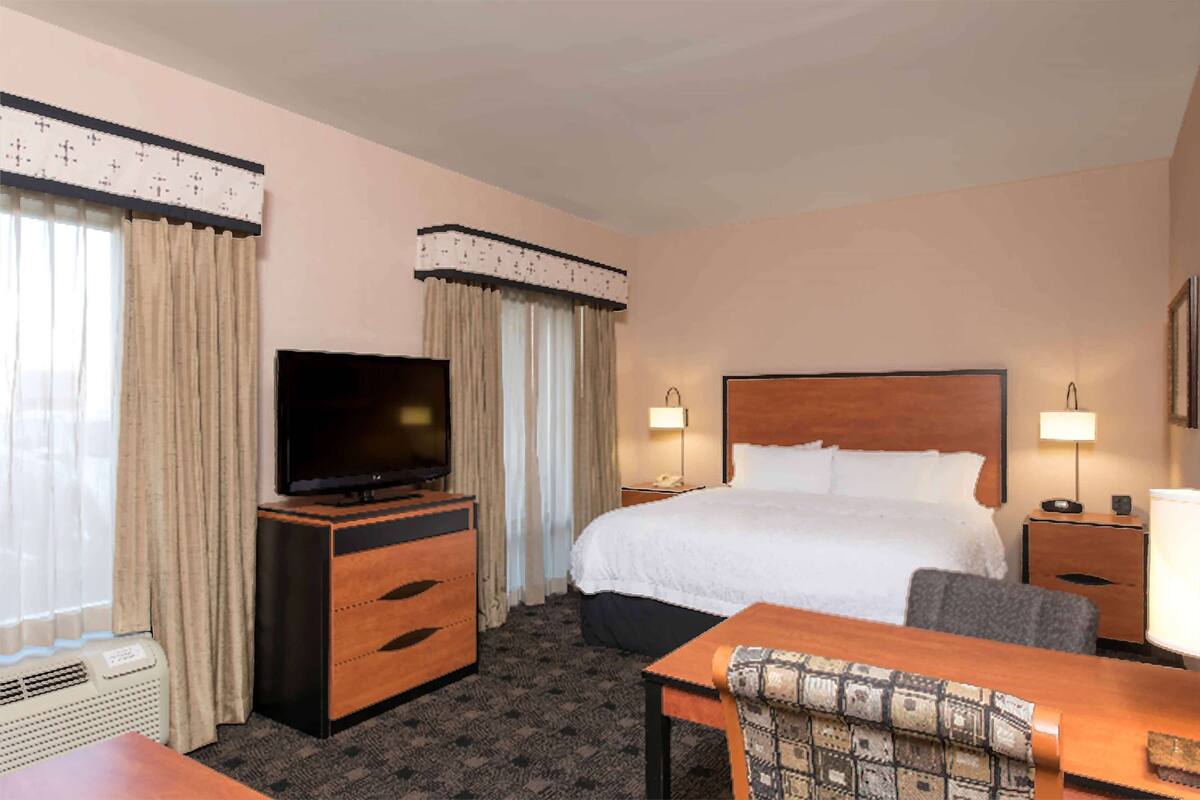 A hotel room with a bed, a TV on a wooden dresser, a desk with a chair, and two bedside lamps.
