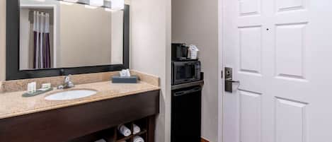 Une salle de bain d’hôtel équipée d’un lavabo, d’un miroir, d’un porte-serviettes et d’un four à micro-ondes.