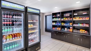 Un mercado luminoso con dispensadores de bebidas refrigeradas y estantes llenos de aperitivos y bebidas.
