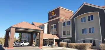 Un hotel con un cartel llamativo de 'Quinlan', un acceso cubierto y un estacionamiento con varios coches.