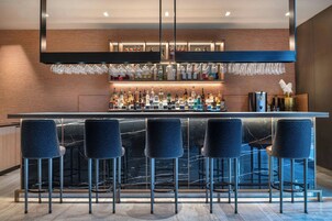 Een bar met een marmeren aanrecht, barkrukken en diverse flessen.
