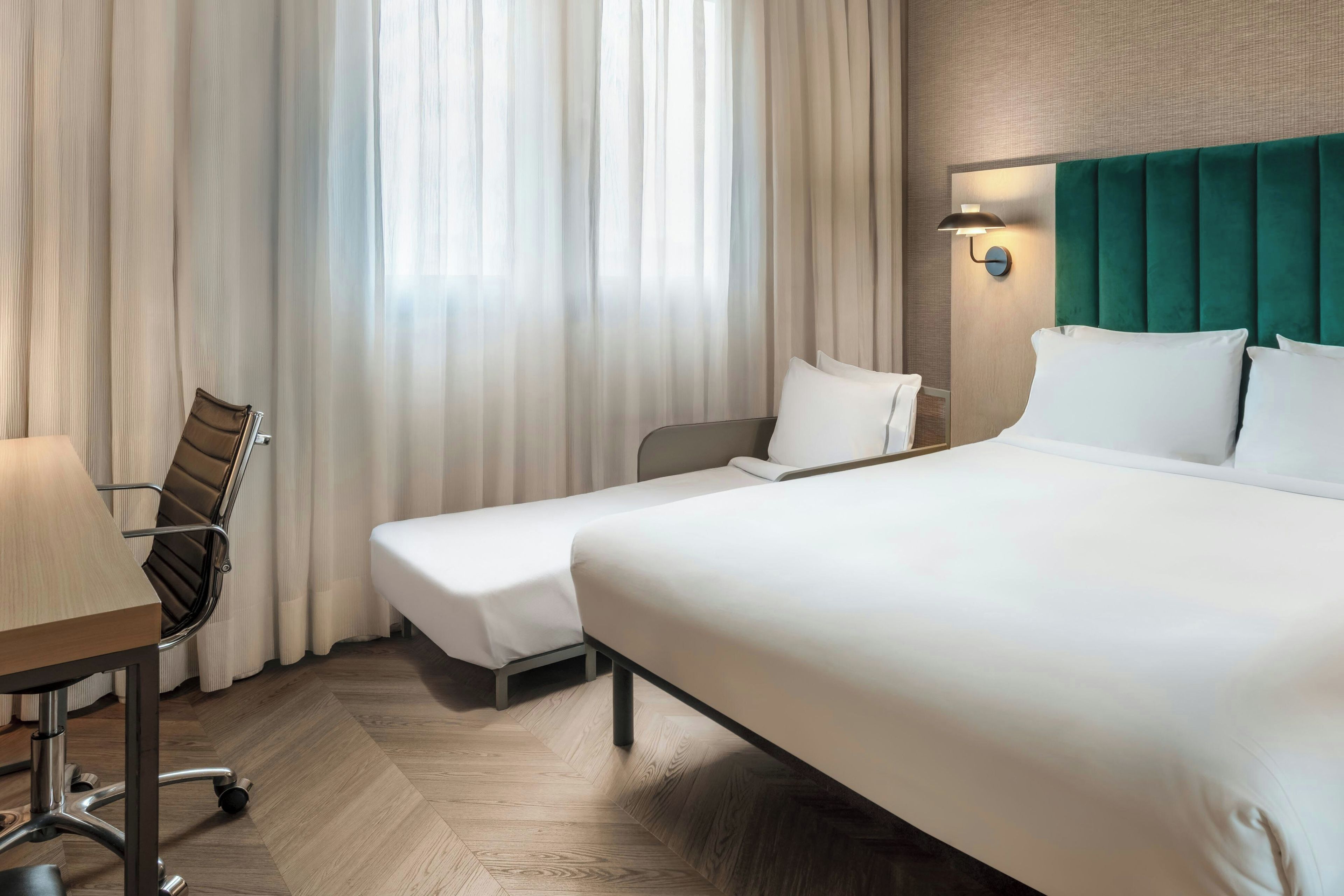 A hotel room with a bed, a desk, and a chair.