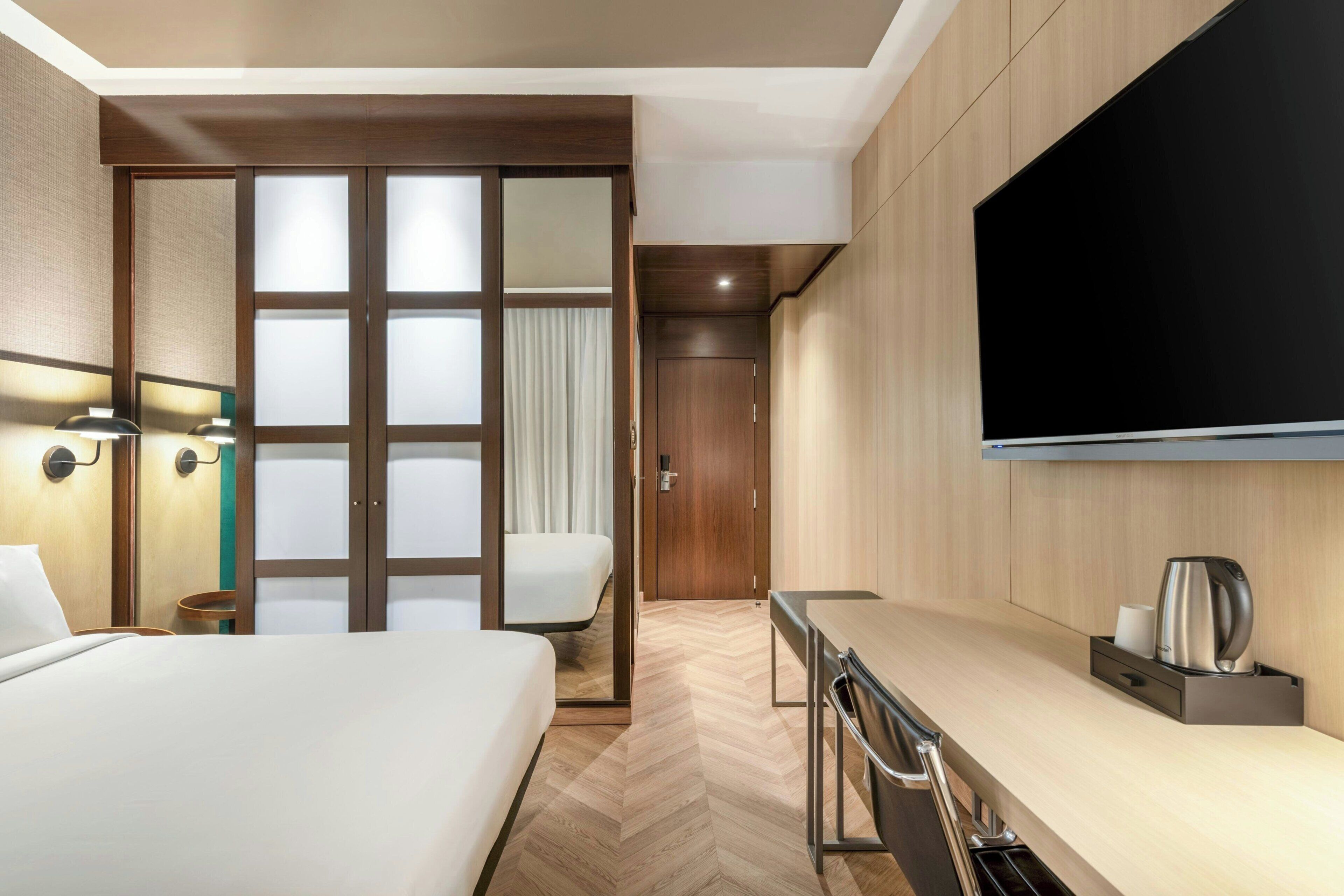 Habitación de hotel con cama, escritorio, silla, televisor y armario.