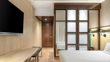 Una habitación de hotel con cama, escritorio, televisión y puerta corredera que da a un baño.