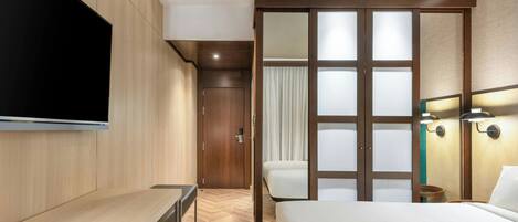A hotel room with a bed, a desk, a TV, and a sliding door leading to a bathroom.