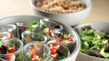 A bowl of salad with cherry tomatoes and greens, a bowl of pasta, and a bowl of mixed greens.